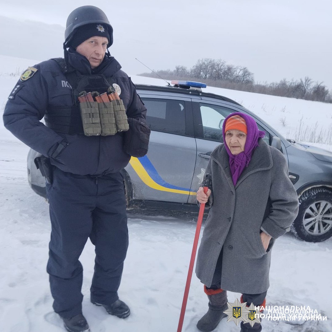 Поліцейський у зимовій формі спілкується з цивільним біля службового автомобіля на засніженій дорозі.