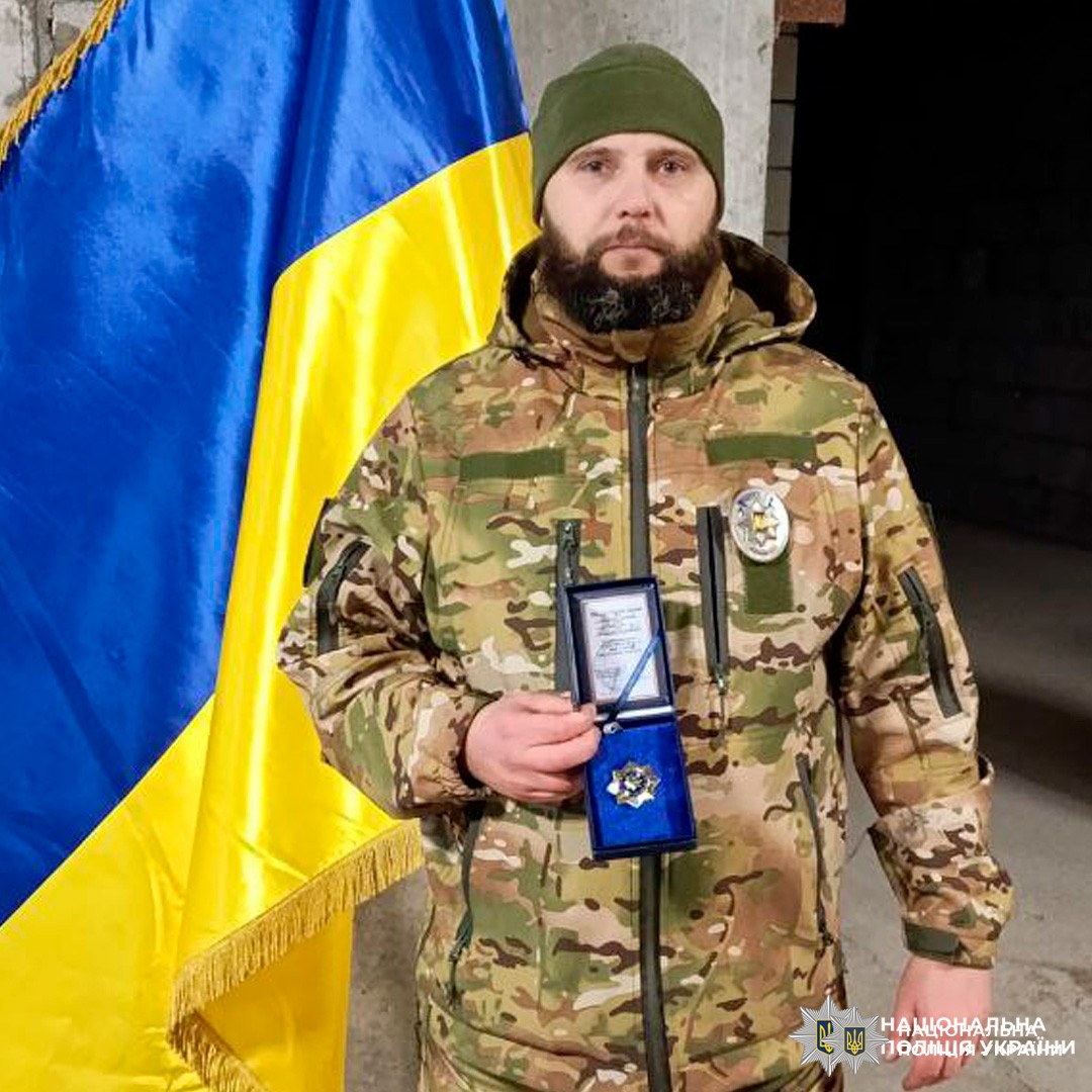 Момент вручення нагороди поліцейському на тлі українського прапора.