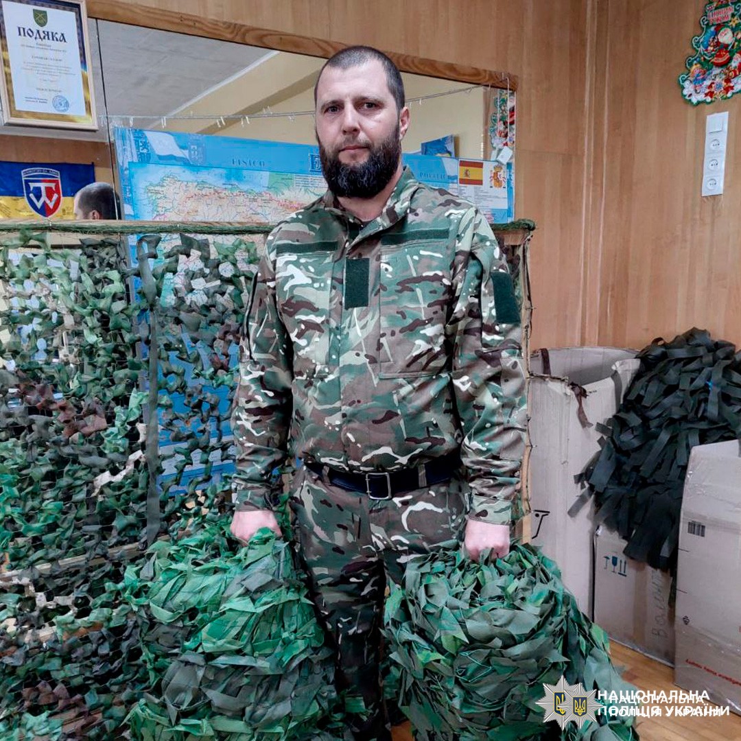 Працівник у камуфляжі тримає маскувальні сітки у приміщенні з коробками та картами.