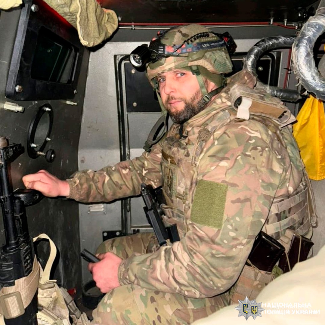 Поліцейський у камуфляжі та шоломі з ліхтариком під час служби в броньованій техніці.