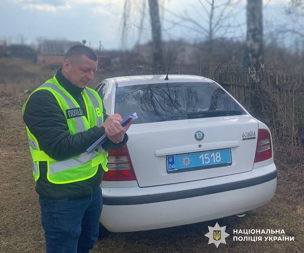 Слідчий поліції стоїть біля службового авто та записує свідчення
