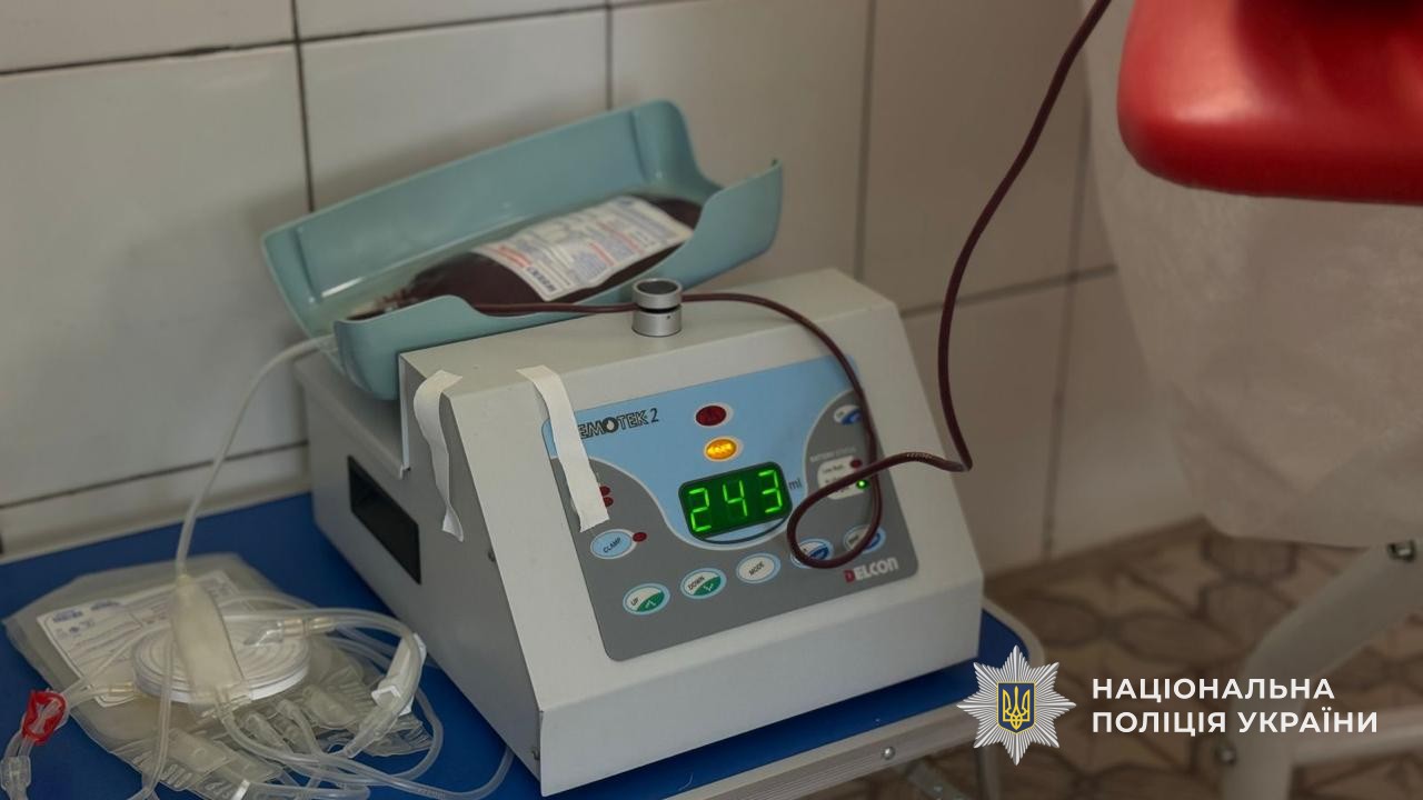 Апарат для забору крові у процесі роботи. На цифровій панелі відображається число 243, зверху на лотку лежить пакет, що наповнюється кров'ю.