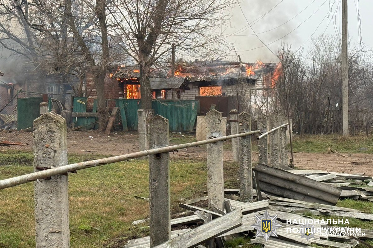 Будинок у Харківській області охоплений вогнем, дах і приміщення палають, густий дим здіймається вгору. На передньому плані видно зруйновану огорожу та уламки.