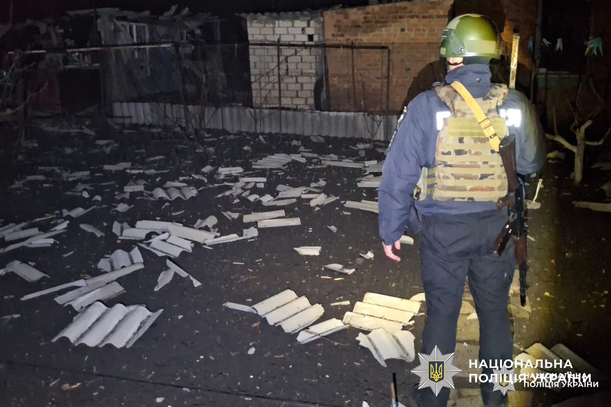 Поліцейський у тактичному спорядженні серед нічних руїн оглядає територію після вибуху.