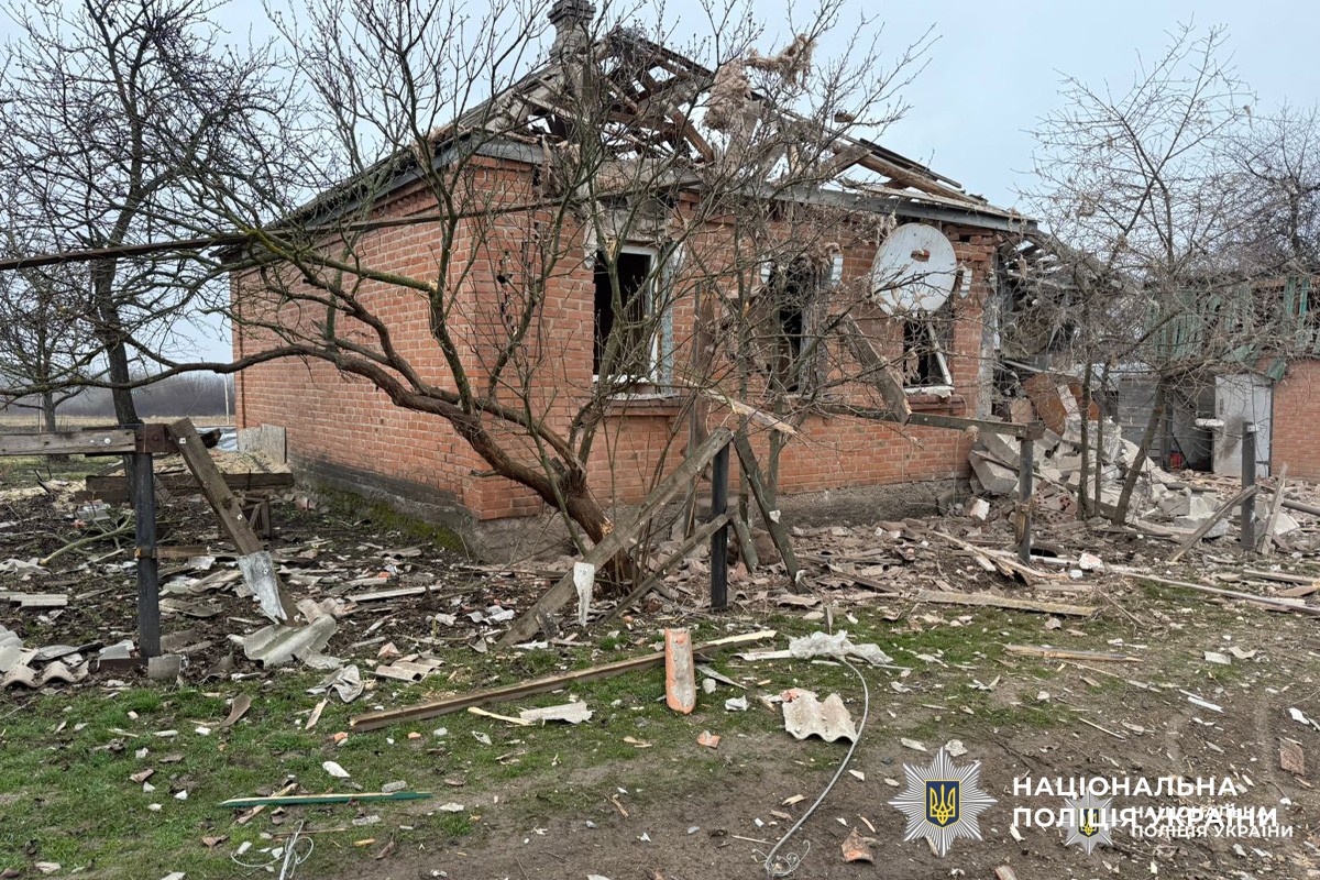 Пошкоджений житловий будинок із зруйнованим дахом та розбитими вікнами, уламки деревини й цегли розкидані на подвір’ї.