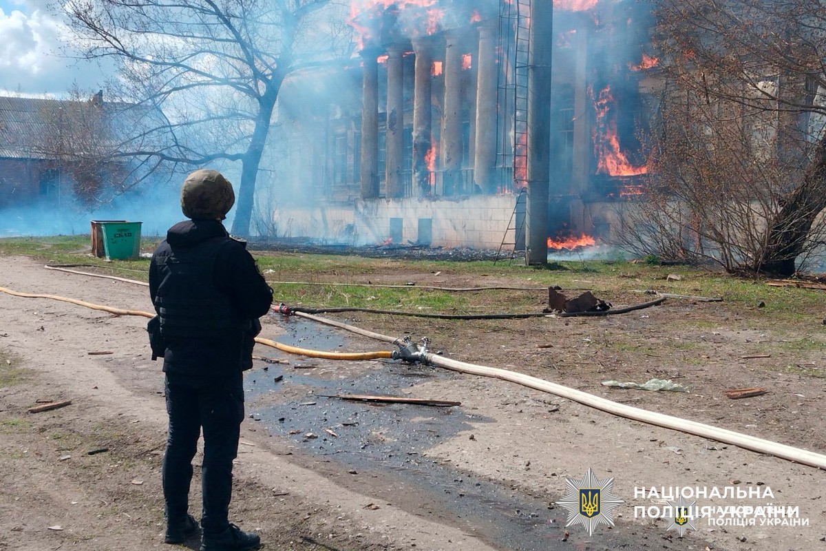 Будівля з колонами охоплена вогнем, зафіксовано масштабне займання. Поліція документує подію.