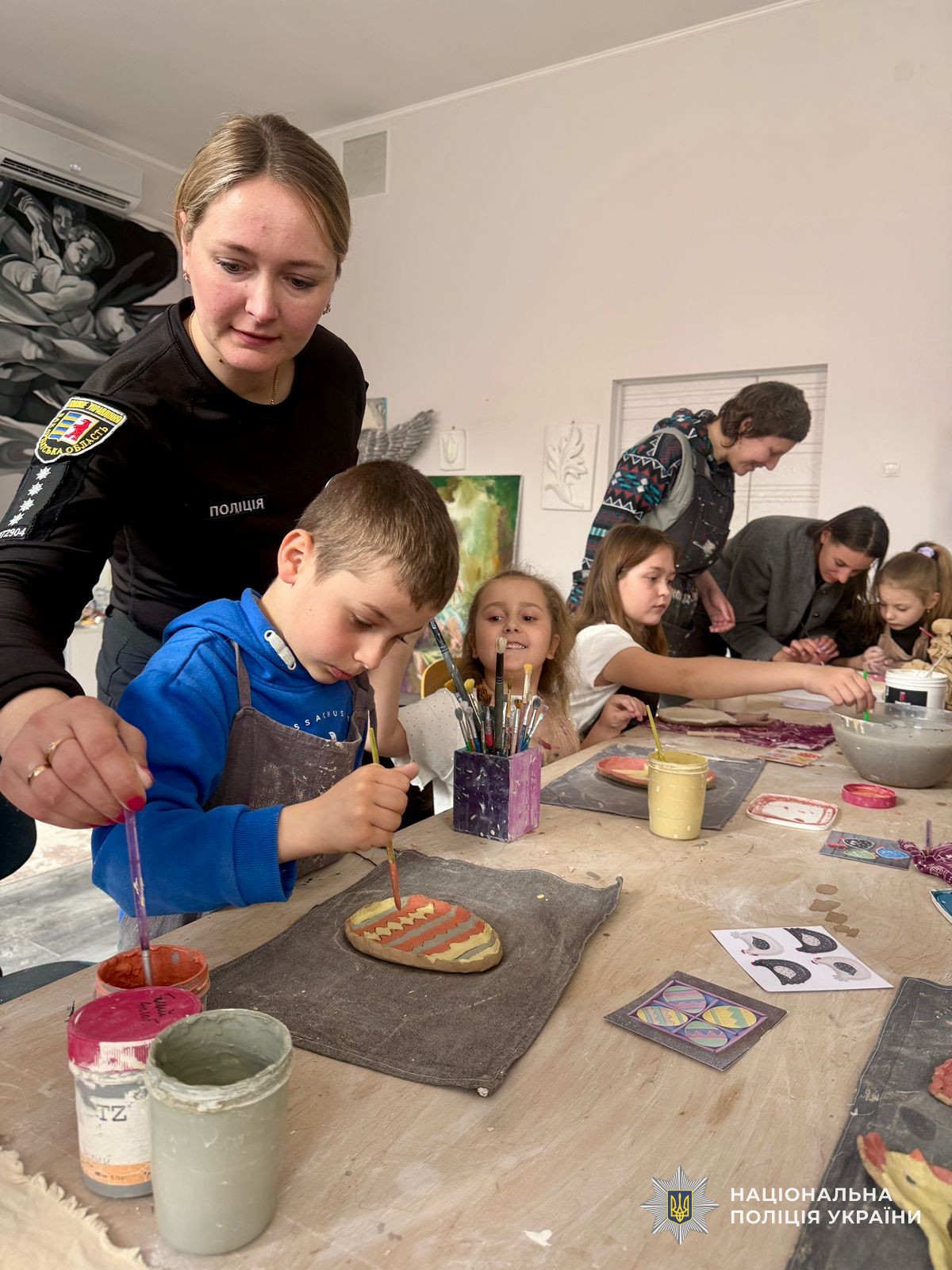 Поліцейська допомагає хлопчику робити виріб із глини